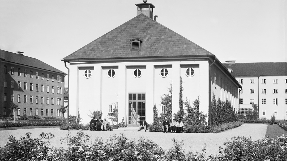 Människor sitter utanför en stor byggnad på en gård.