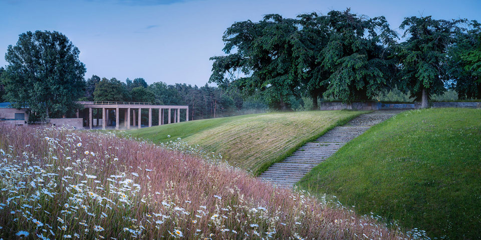 Grön kulle med träd och en byggnad i bakgrunden, som skapar en harmonisk och naturskön miljö.