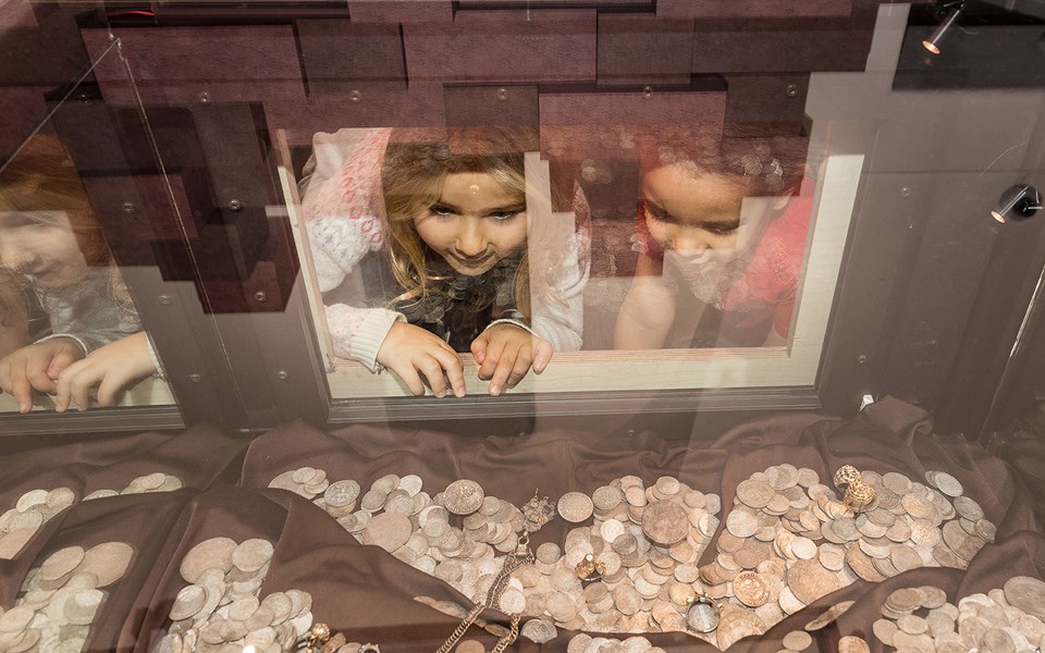 Barn tittar nyfiket på en stor samling blänkande mynt.