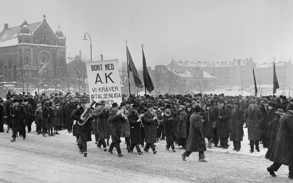 Demonstrationståg med plakat, fanor och blåsorkester.